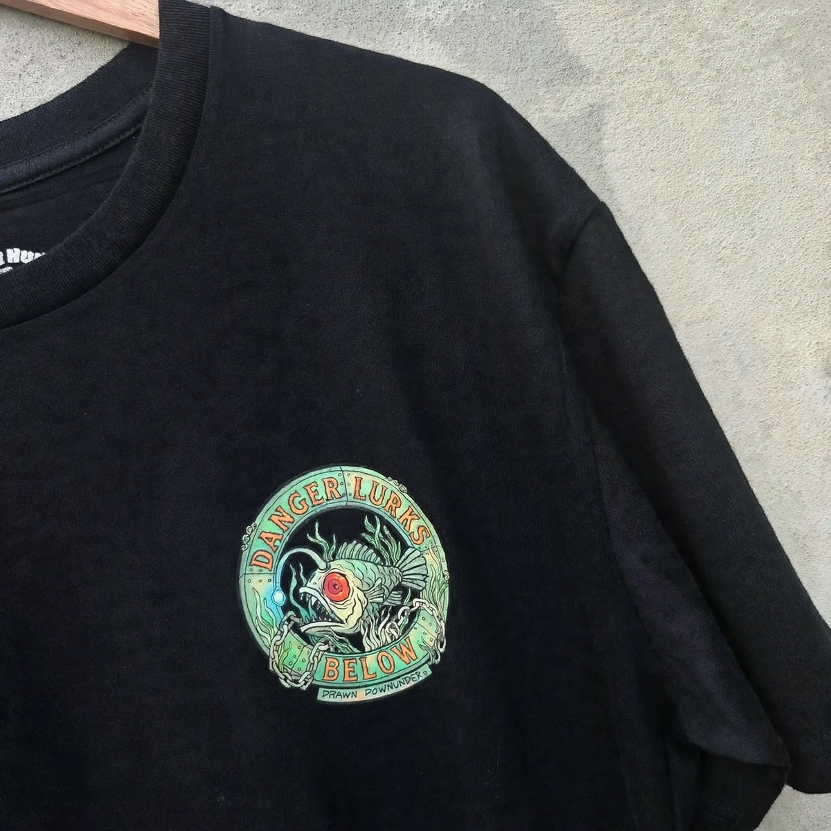 Bad Buoys angler fish pocket logo front - Danger Lurks Below chest print on black t-shirt - Drawn Downunder