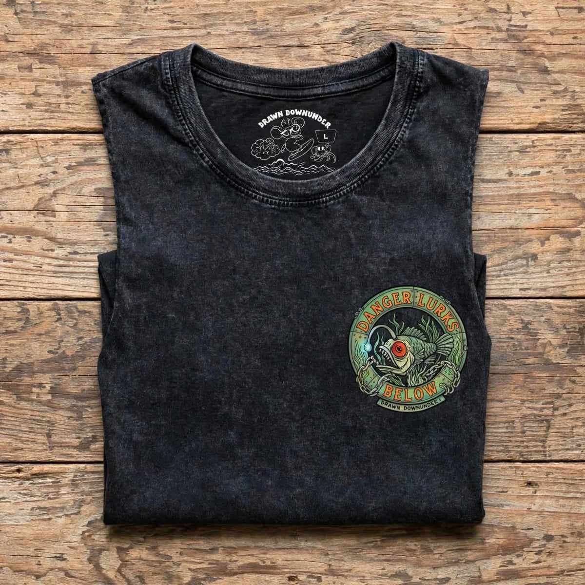 Bad Buoys black stonewash tank folded flat lay - Danger Lurks Below front pocket graphic with Drawn Downunder label size L visible